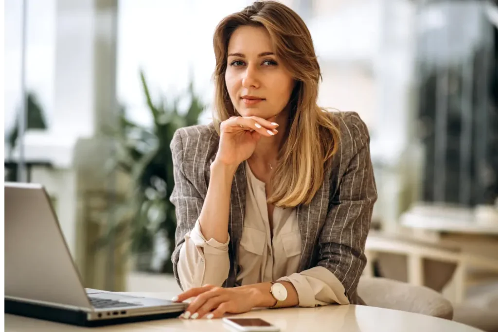 Mulher loira debruçada sobre uma mesa de escritório. Sobre ela, um laptop