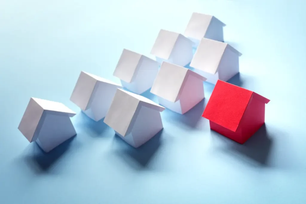 casas de papel branco atrás de uma casa de papel vermelho, sobre uma mesa azul