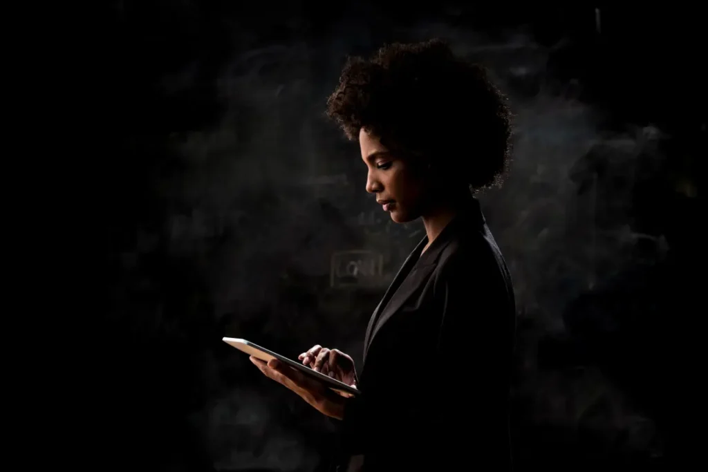 Mulher negra com tablet na mão, em ambiente escuro