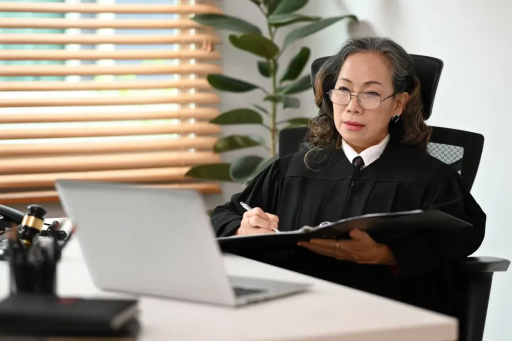juiz asiática com pasta de documentos na mão, fazendo anotações em sua mesa, olhando para um laptop